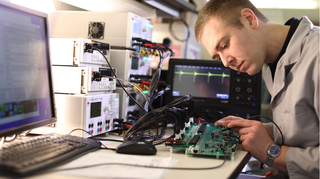 Engineer testing circuit board, oscilloscope shows waveform.